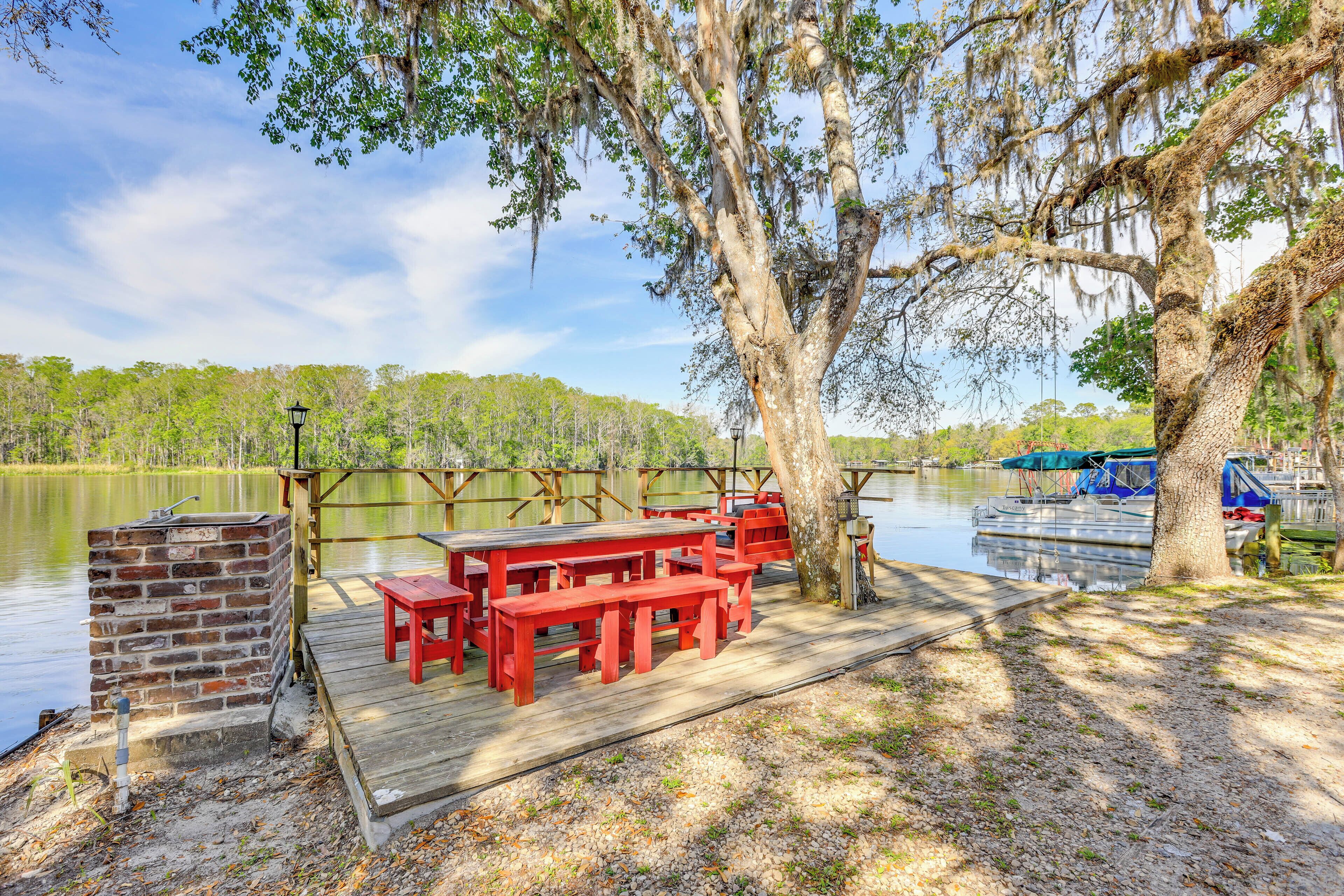 Une jetée en bois avec des bancs rouges et un barbecue en briques, au bord d’un lac paisible.
