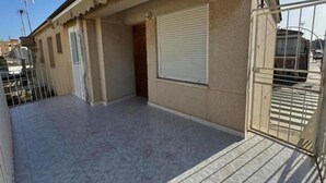 A building with a tiled patio, a closed shutter, and a metal gate.