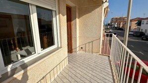 A balcony with a view of the street, a door, and a window with a metal grill.