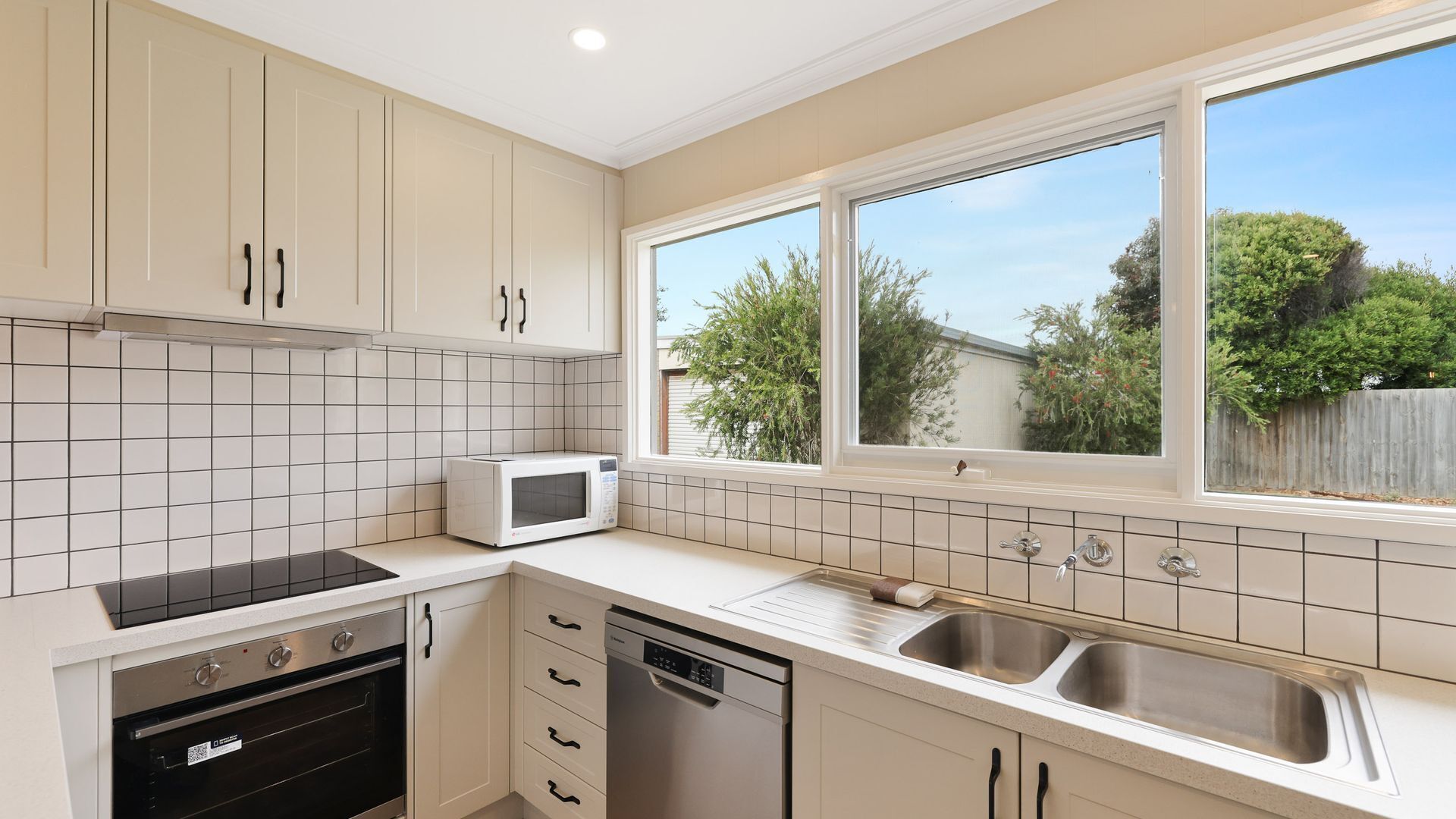 Cocina moderna con armarios blancos, horno empotrado, lavavajillas, microondas y un amplio ventanal con vistas al exterior.