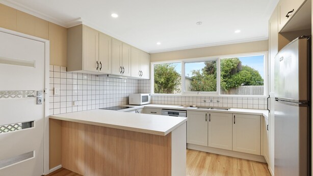 A modern kitchen with white cabinetry, a central island, a built-in microwave, and a large window providing a view of greenery outside. - Avalon Cape Woolamai (Cape Woolamai)