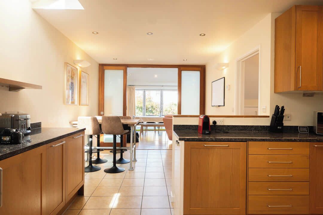 A modern kitchen with wooden cabinets, a countertop with appliances, and a dining area with chairs and a table.