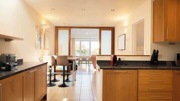 A modern kitchen with wooden cabinets, a countertop with appliances, and a dining area with chairs and a table.
