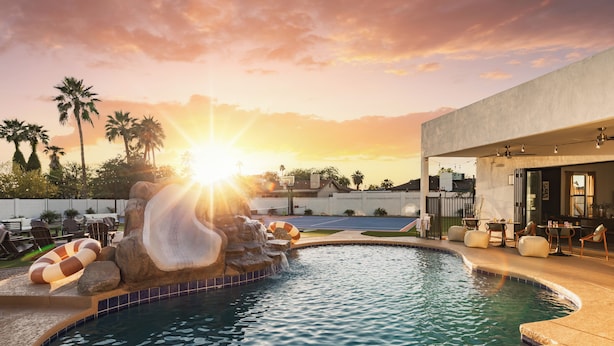 A pool with a waterfall feature, lounge chairs, and a modern building in the background. - Bespoke Playhaus of Scottsdale: Open Sky Estate (Scottsdale)