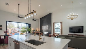 A modern kitchen with a large island, a dining area with a pool view, and a living room with a large TV and comfortable seating. - Bespoke Playhaus of Scottsdale: Open Sky Estate (Scottsdale)
