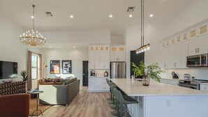 A modern kitchen with white cabinets, a large island with bar stools, a built-in oven, and a microwave. - Bespoke Playhaus of Scottsdale: Open Sky Estate (Scottsdale)