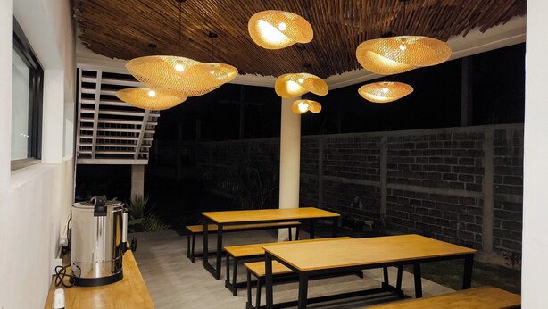 An outdoor dining area with wooden tables and chairs, a coffee machine, and hanging wicker lamps. - Bunkhouse Koh Phangan (Ko Pha-ngan)