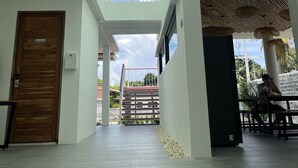A spacious indoor area with a high ceiling and a glass roof, leading to an outdoor area with a staircase and a view of greenery. - Bunkhouse Koh Phangan (Ko Pha-ngan)