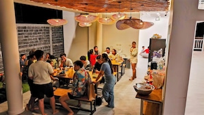 A dining area with multiple tables and chairs, a brick wall, and hanging pendant lights. - Bunkhouse Koh Phangan (Ko Pha-ngan)