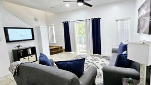 Ein Wohnzimmer mit grauen Sofas, einem Flachbildfernseher, einer kleinen Kommode und einem gemusterten Teppich.