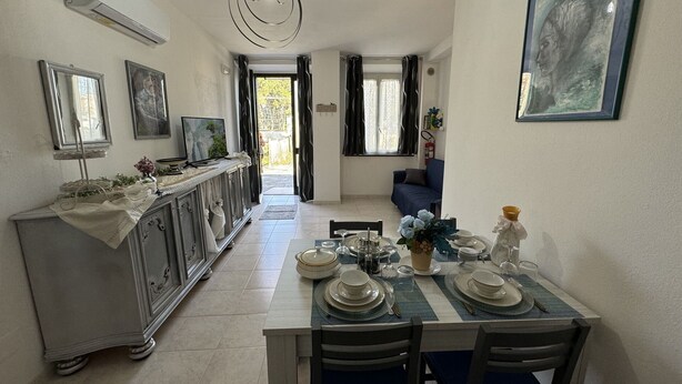 A dining area with a table set for four, a kitchen in the background, and a view through an open door. - Country House / Farm House in Vecchiano-nodica with 1 bedrooms sleeps 3 (Vecchiano-nodica)