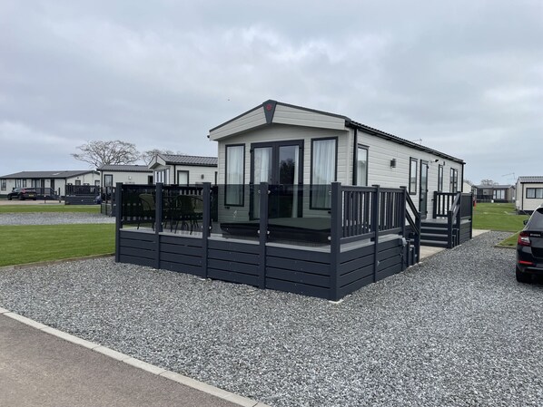 A mobile home with a deck and a covered porch, surrounded by gravel and grass.