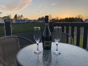 Une table avec une bouteille de vin Santi Nello et deux verres, placée sur un balcon donnant sur une route et des maisons.