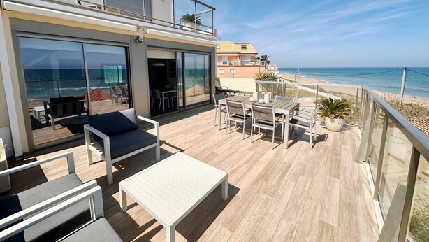 Un balcón moderno al aire libre con vista a la playa, amueblado con una mesa, sillas y un sofá.