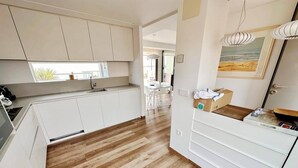 Una cocina moderna con armarios blancos, suelo de madera y una zona de comedor visible al fondo.