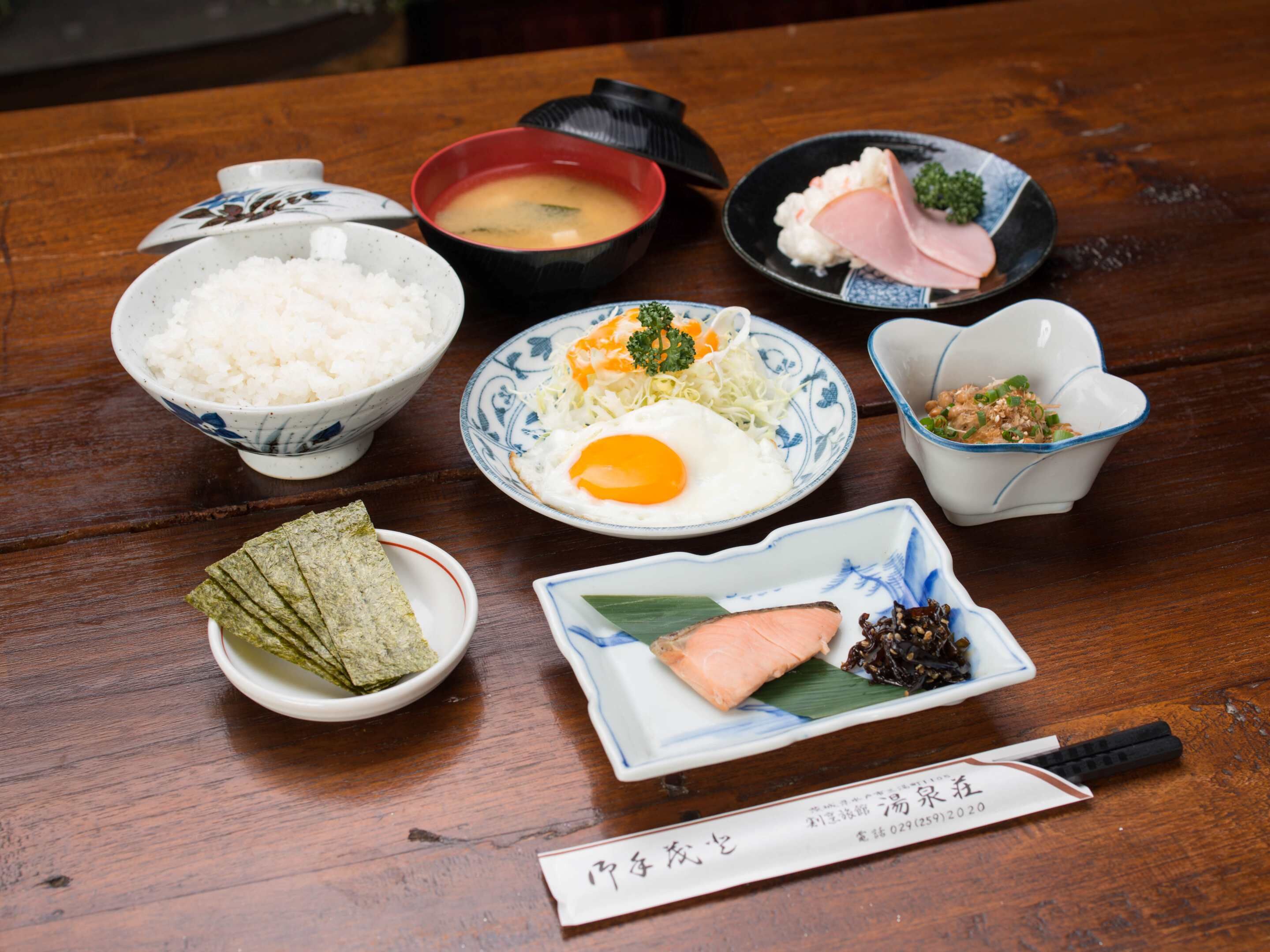 A wooden table with various dishes including rice, soup, a plate with an egg, and a plate with salmon.