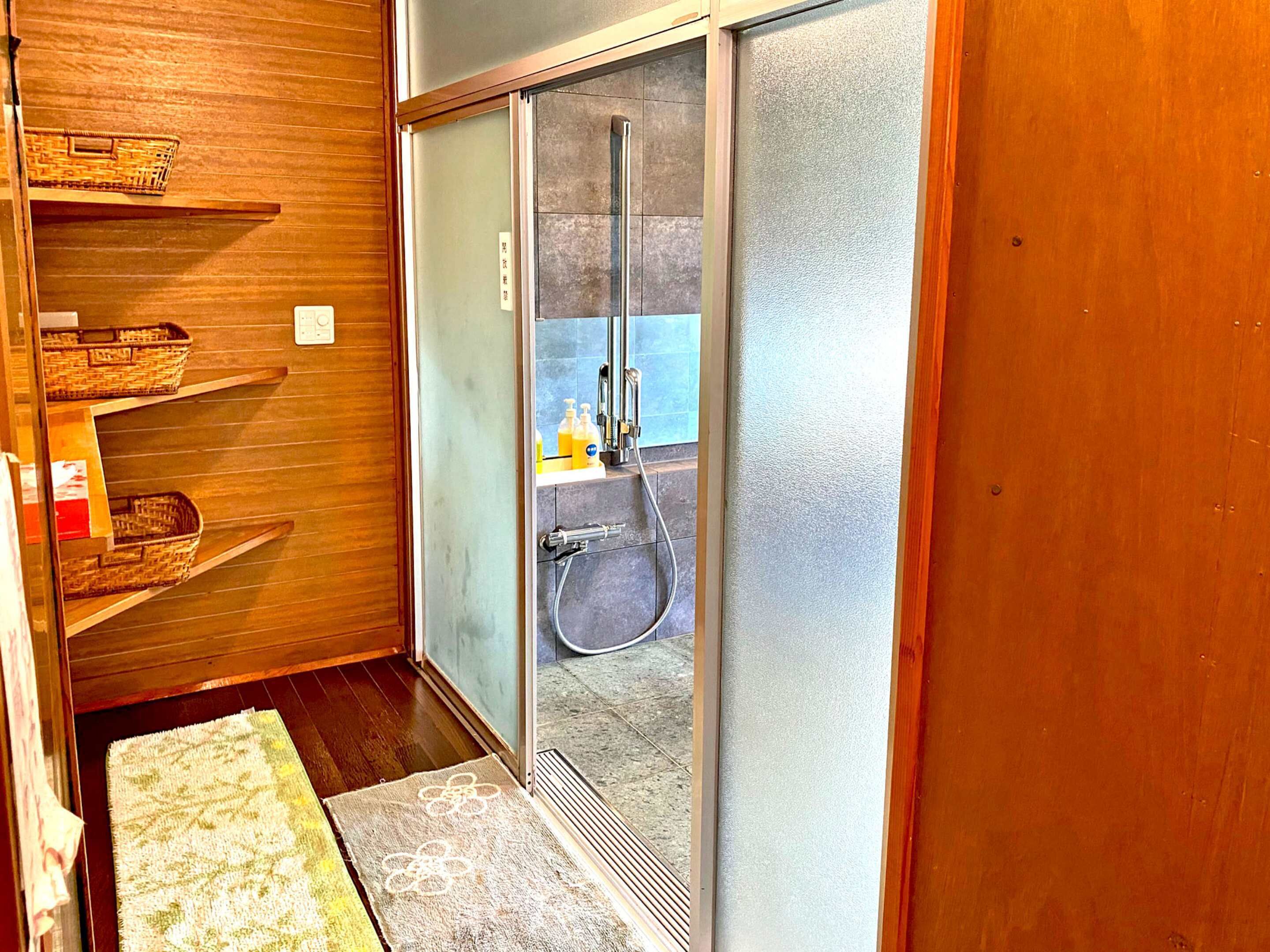 A compact bathroom with a shower, wooden shelves, and a small sink area.