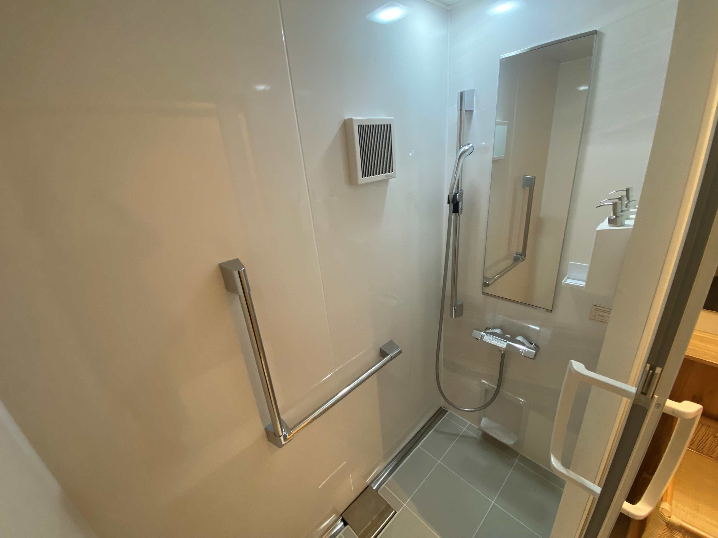 Un baño moderno con cabina de ducha de vidrio, ducha de mano, inodoro de pared y espejo.