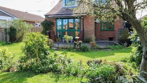 Une maison en briques avec une porte verte, un petit jardin et un arbre au premier plan.