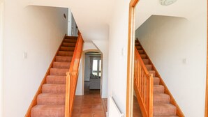 Un escalier avec des rampes en bois et des marches recouvertes de moquette, menant à l’étage supérieur.