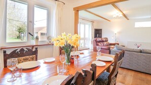 Un coin repas avec une table en bois dressée pour quatre personnes, un vase rempli de fleurs jaunes et une vue sur le jardin grâce à de grandes fenêtres.