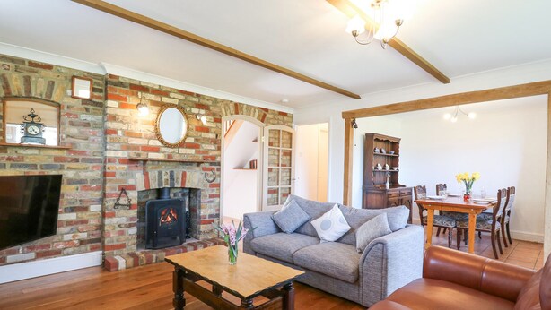 Un salon avec une cheminée en briques, un canapé, un divan en cuir, une table basse en bois et un coin repas avec une table et des chaises.