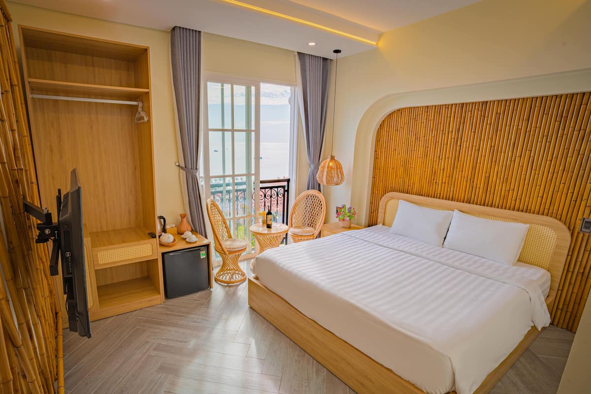 A hotel room with a large bed, a small desk, a chair, a balcony view, and a wardrobe.