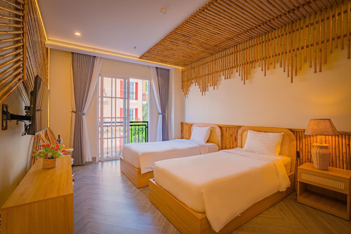 A hotel room with two beds, a wooden headboard, a nightstand, and a window with curtains.