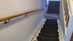 Una escalera con barandilla de madera y un rellano cubierto de alfombra negra.