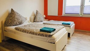 Habitación con dos camas, cada una con ropa de cama y almohadas estampadas, una ventana con persianas y una pared roja.