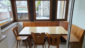 Un comedor con una mesa y sillas de madera, ventanas amplias y un banco a lo largo de la pared.