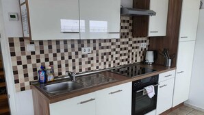 Una cocina moderna con armarios blancos, salpicadero de azulejos, un lavamanos de acero inoxidable, estufa y cafetera.