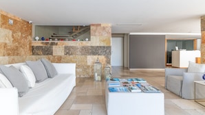 Una sala de estar moderna con una pared de acento de piedra, un sofá blanco, una mesa de centro con revistas y un mostrador de recepción al fondo.