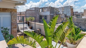 Una terraza en la azotea con zona de estar, plantas en macetas y vistas de los edificios circundantes.