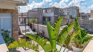 A rooftop terrace with a seating area, potted plants, and a view of surrounding buildings.