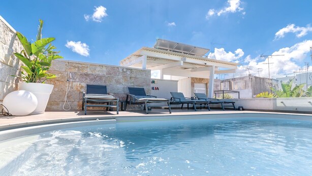 Una piscina con sillones de descanso y una pérgola.
