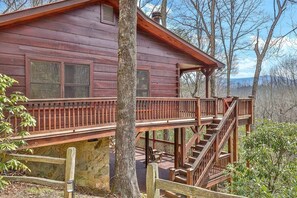 Una cabaña con terraza de madera, una escalera y vistas del bosque circundante.