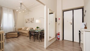 A modern living room with a glass dining table, beige sofa, and a ceiling light fixture. - Stylish 2-Bedroom Flat by St. Peter’s – King Bed, A/C, Fast Wi-Fi. Super Clean! (Roma)