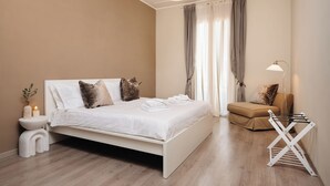 A bedroom with a bed, bedside table, lamp, and a small seating area. - Stylish 2-Bedroom Flat by St. Peter’s – King Bed, A/C, Fast Wi-Fi. Super Clean! (Roma)