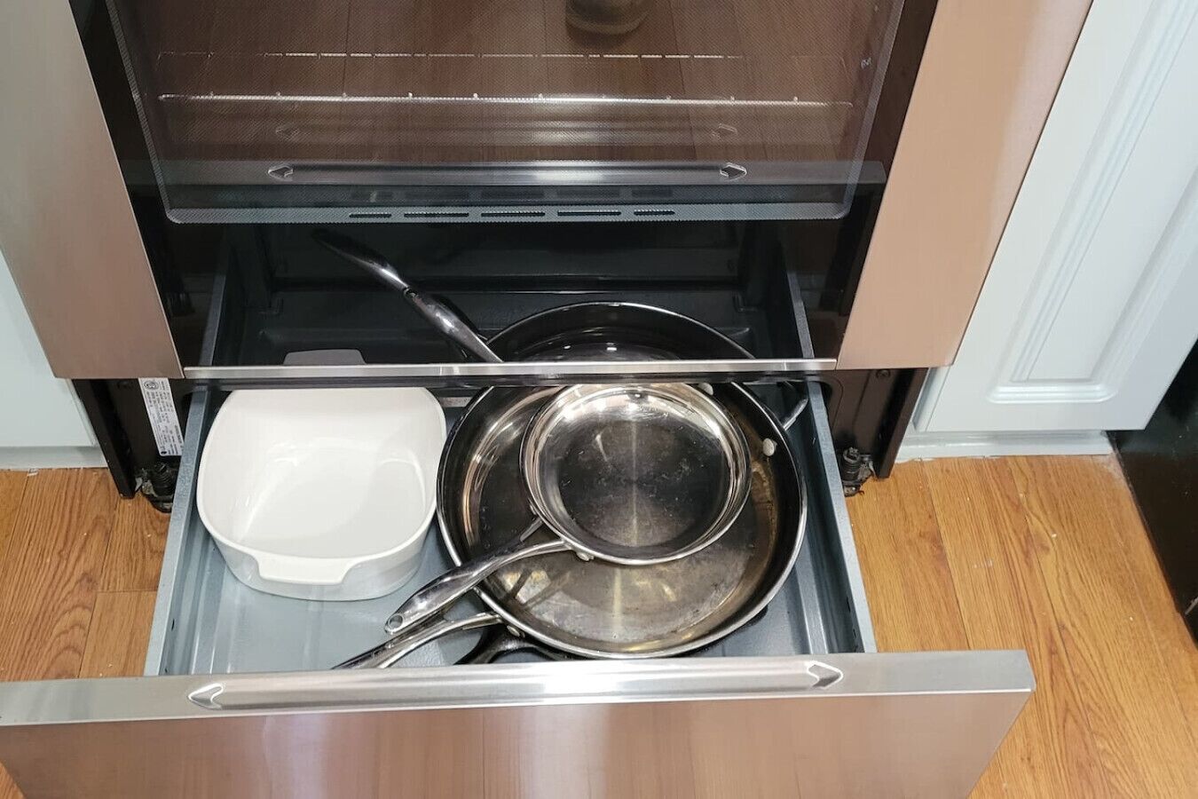 Een keukula open met een witte schaal, een roestvrijstalen pan en een zwarte ovendeur.