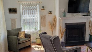 Een woonkamer met een bank, een fauteuil, een open haard en een televisie.