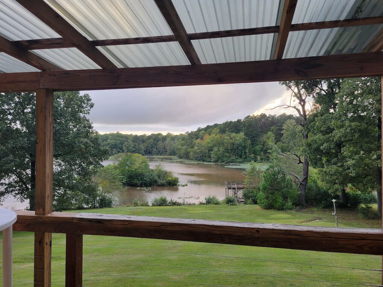 A covered outdoor area with a view of a lake surrounded by trees.