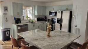 Een moderne keuken met lichtblauwe kastjes, roestvrijstalen apparatuur, een marmeren eiland en een eethoek met bruine stoelen.