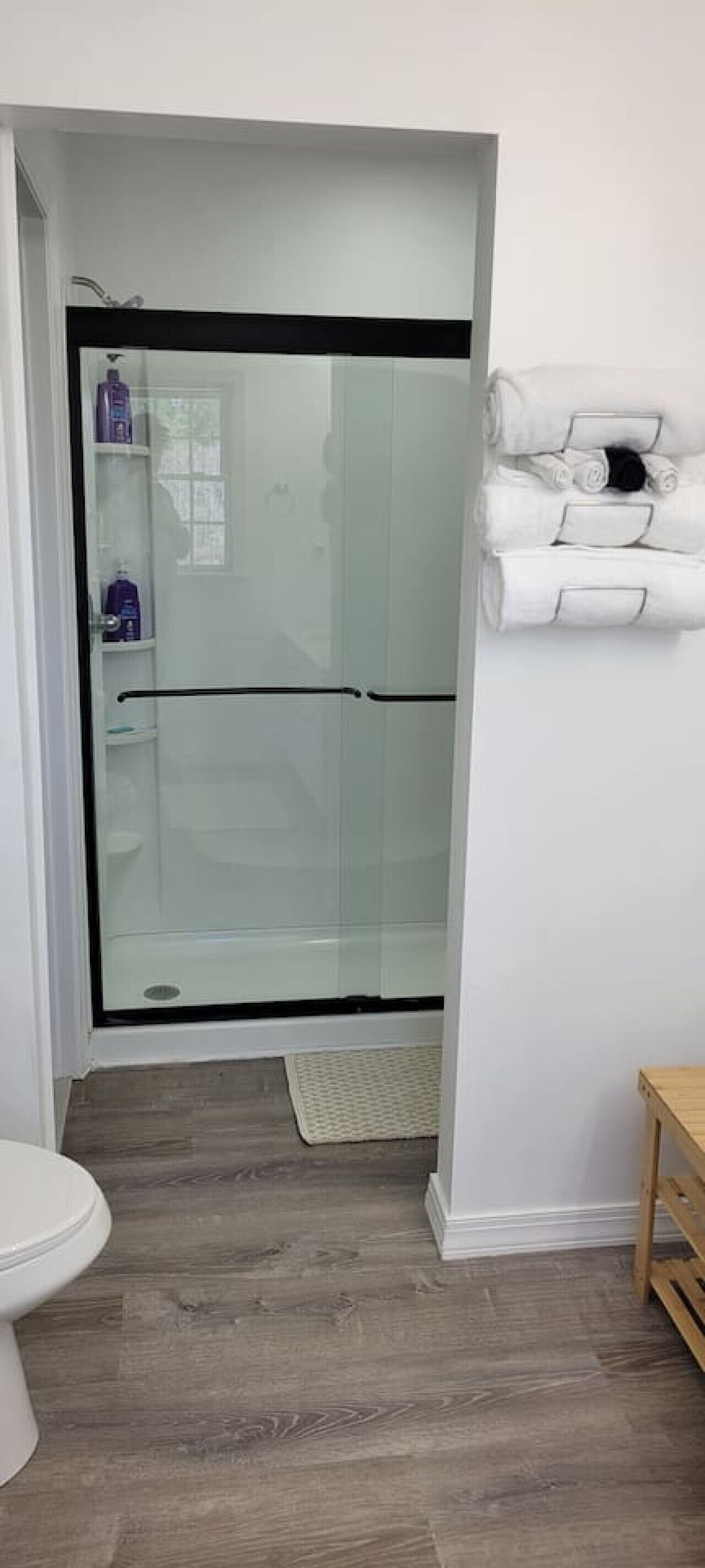 Une salle de bain moderne avec une douche à parois de verre, des toilettes blanches et des serviettes soigneusement pliées sur une étagère.