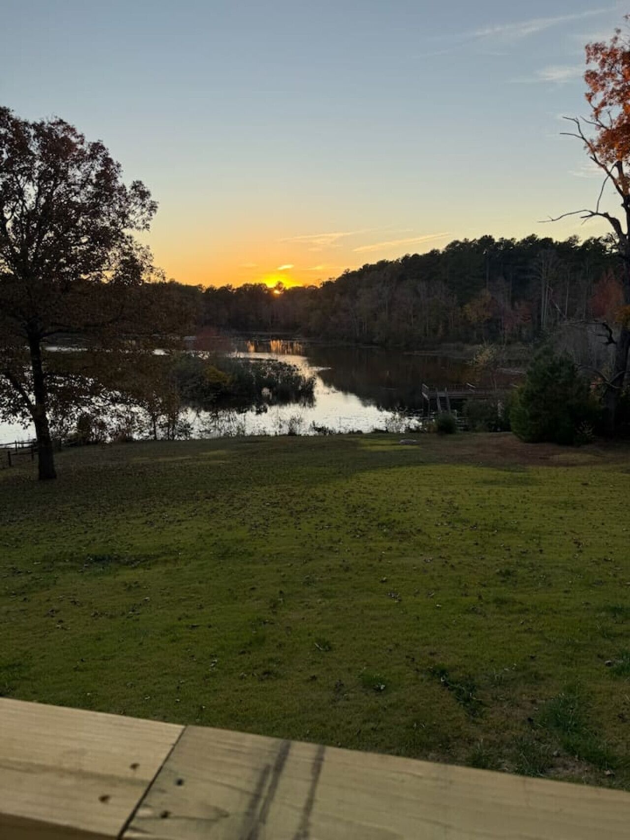 A grassy area with a body of water reflecting the sunset.