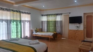 A hotel room with a large bed, a smaller bed, a wooden wardrobe, a television mounted on the wall, and a wooden door. - The Latsas (Hunder)