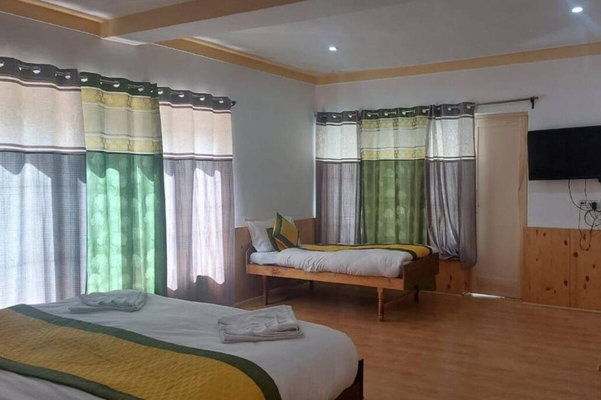 A hotel room with a large bed, a smaller bed, a wooden wardrobe, a television mounted on the wall, and a wooden door.