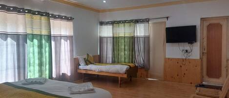 A hotel room with a large bed, a smaller bed, a wooden wardrobe, a television mounted on the wall, and a wooden door.