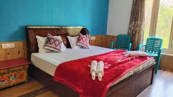 A neatly made bed with a red blanket and two towels, a wooden headboard, and a small wooden chest of drawers.