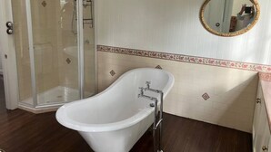 A bathroom with a freestanding bathtub, a glass-enclosed shower, and a wall-mounted mirror. - Library Cottage (Hamilton)
